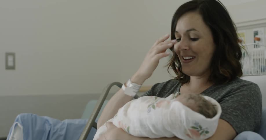 A young woman sits in a hospital bed holding her newborn baby