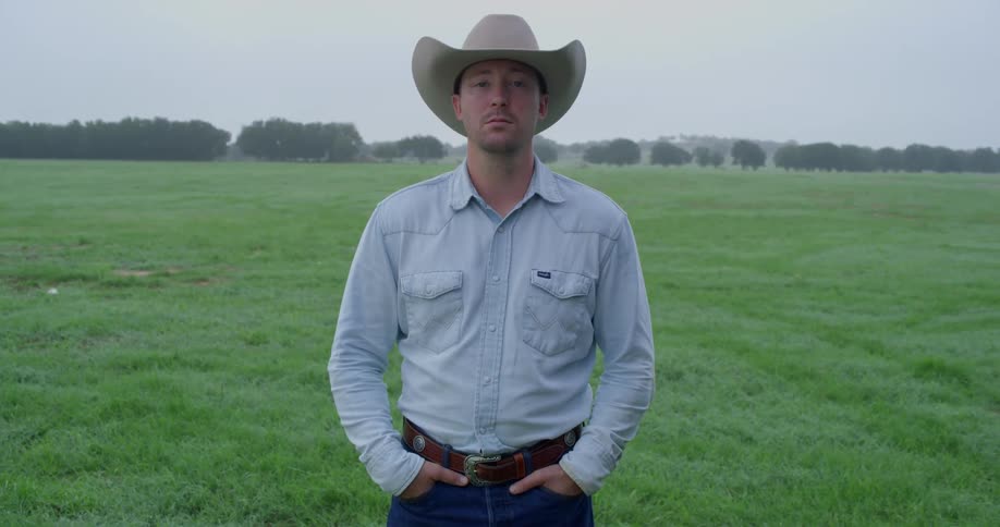 Man wearing a cowboy hat stands in a wide open field
