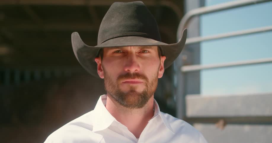 Man wearing a cowboy hat looks at the camera at the stable