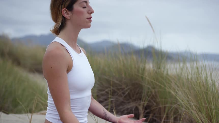 A woman sitting on the sand in the beach meditating