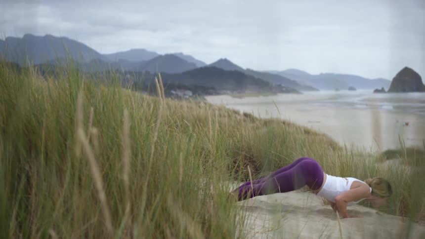 Woman works through yoga poses on sand near beach