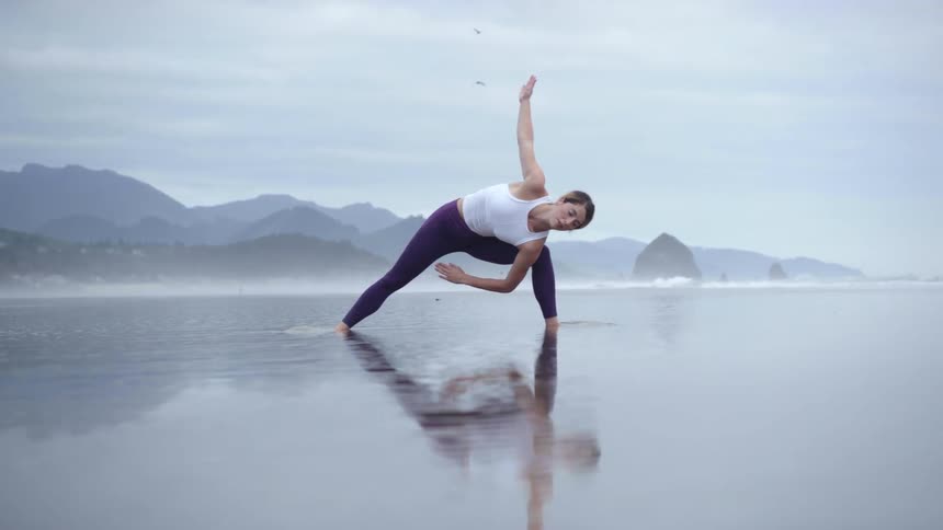 A woman does yoga while standing on a foggy beach