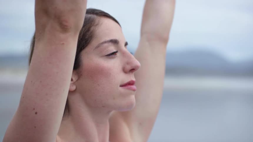A woman stretches while standing on a beach smiling