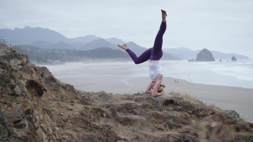 A woman is doing yoga outdoors by the coast of a beach