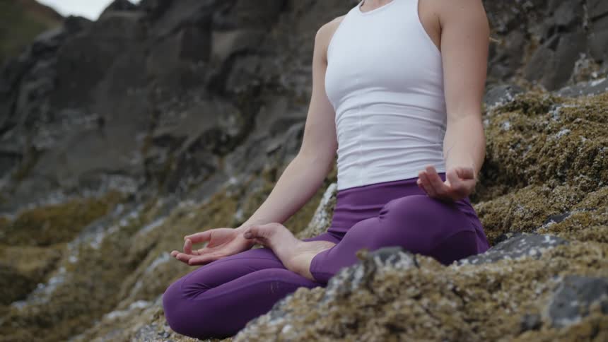 A woman sitting on rocks and seaweed meditating