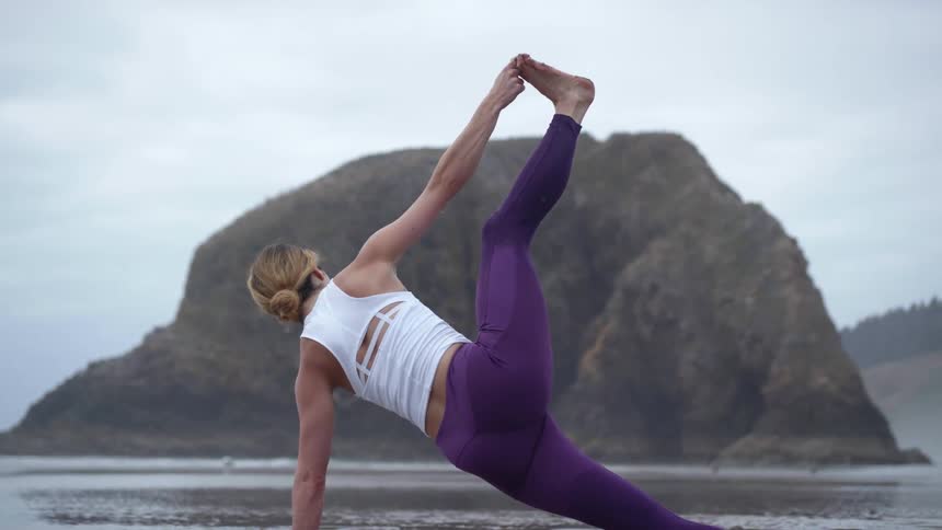 A woman is doing yoga in the wet sand of the beach