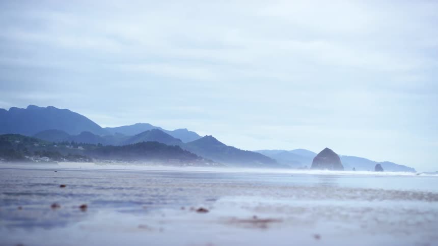 A beach with waves and mountains in the background