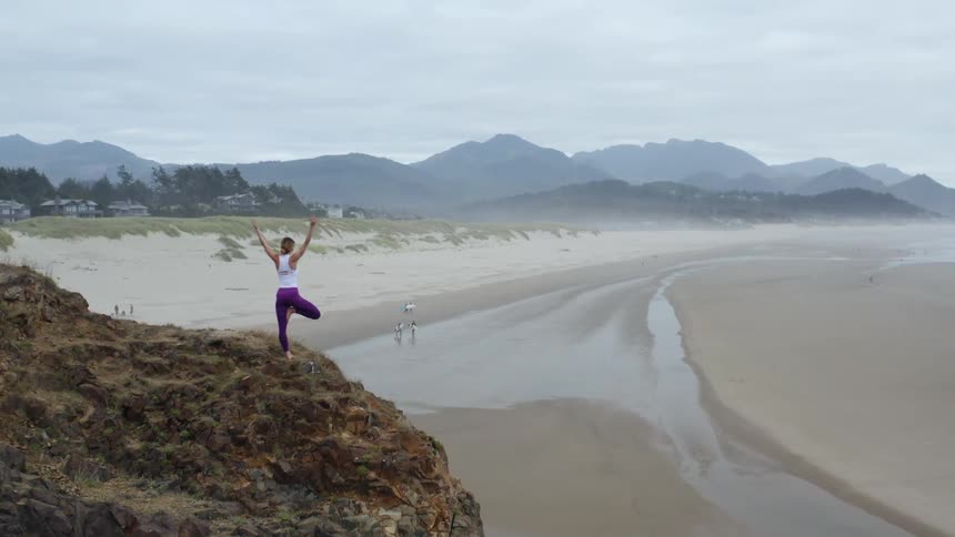 A woman doing yoga on a cliff overlooking a beach