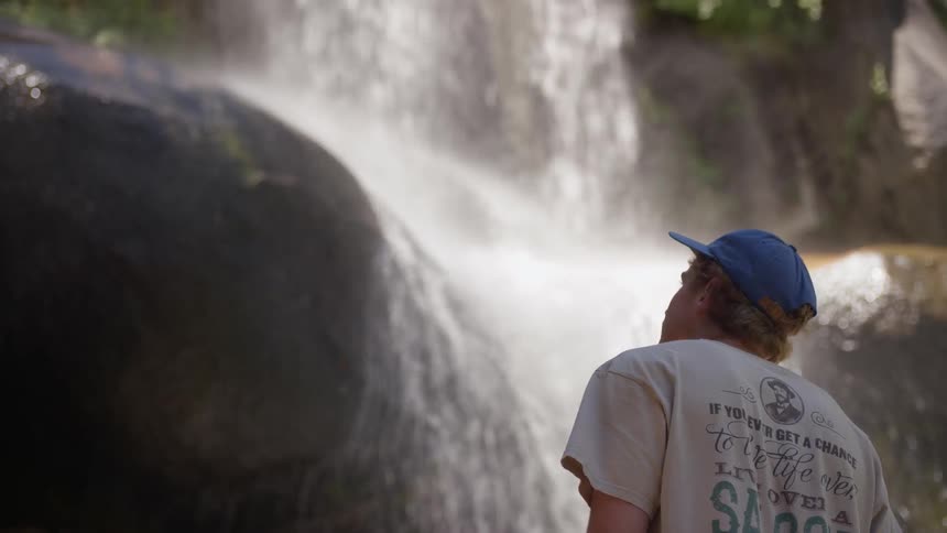 A man in a ball cap looking up at a waterfall