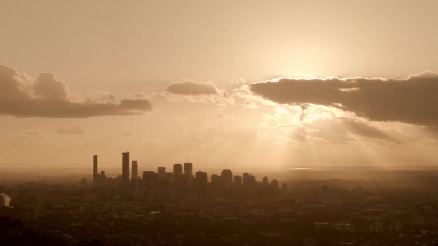 Aerial footage of a city and its skyline as sunbeams stream through clouds