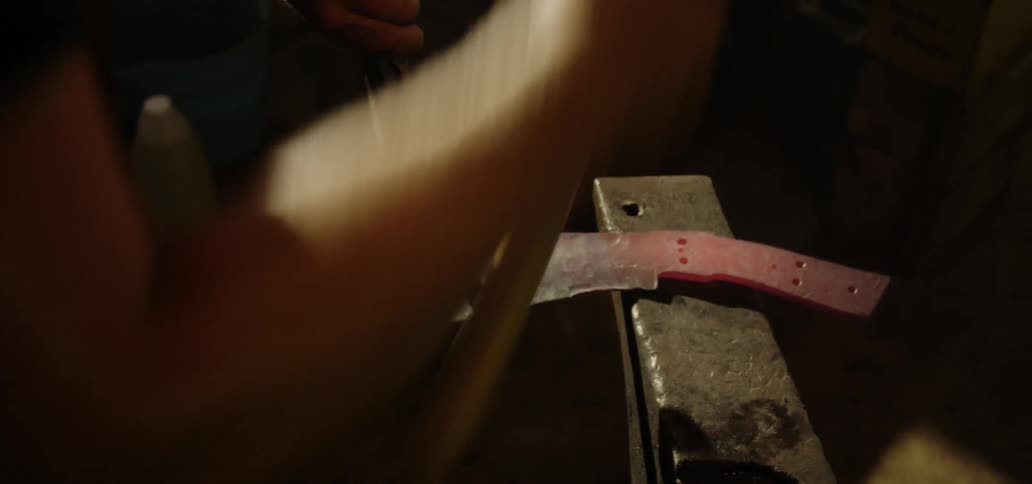 A blacksmith beats a piece of heated metal on an anvil