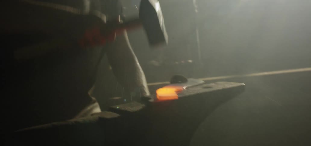 A blacksmith hammering a piece of molten metal on an anvil