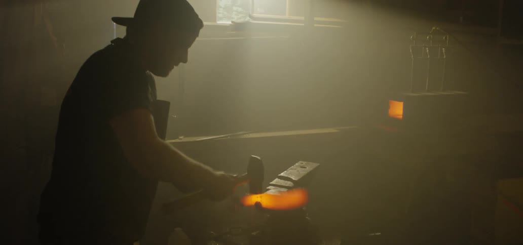 A man uses a mallet and hits a fire red piece of hot iron