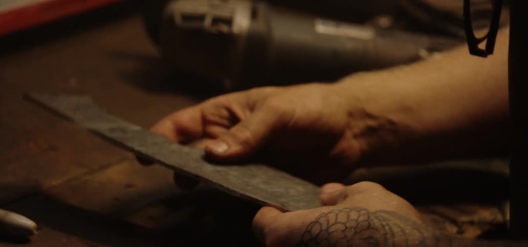 A blacksmith checks the blade of a steel knife