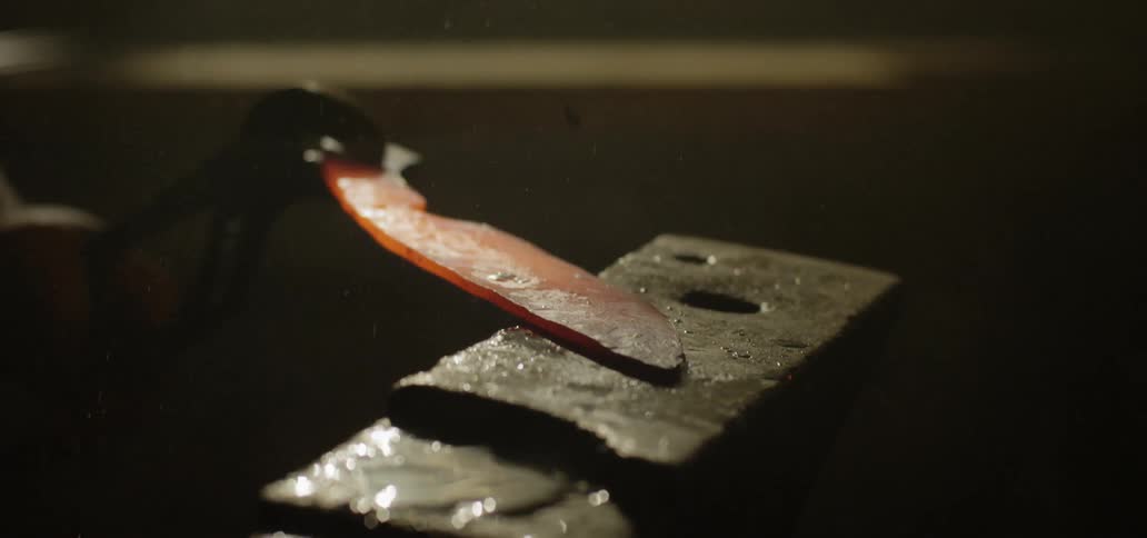 A blacksmith slams his hammer onto hot metal on an anvil