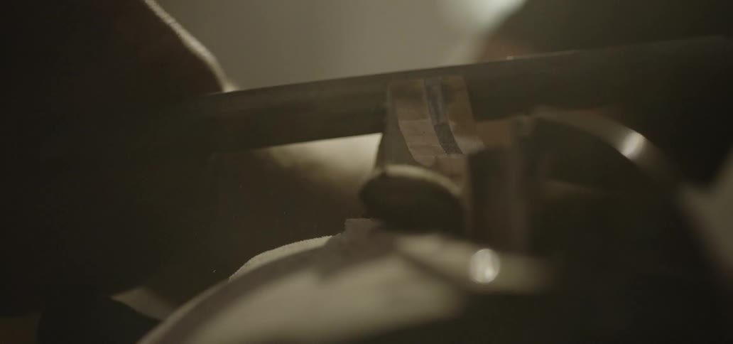 A person guides a filing tool back and forth across a piece of metal to smooth it