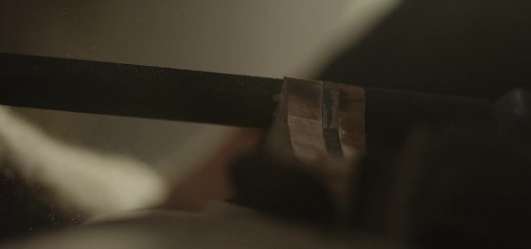 A man rubs a metal tool against block of wood