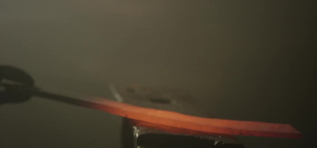 A blacksmith beats a hot piece of metal with a hammer