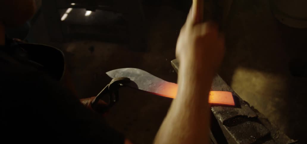 A blacksmith hammers on a hot knife
