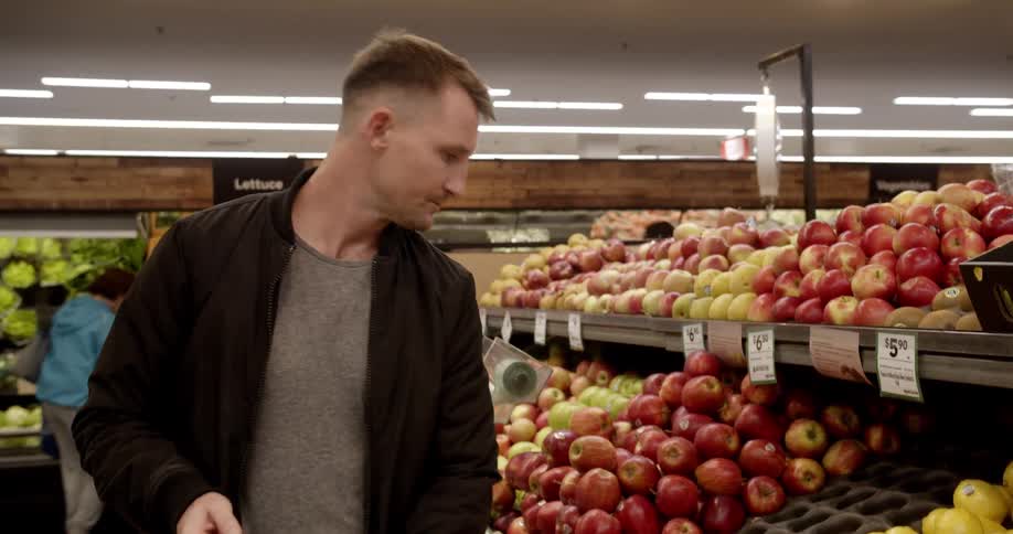 A man placing an apple into a shopping basket