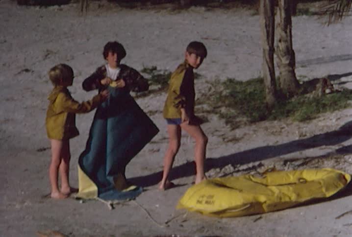 Three boys airing up a water raft by a lake