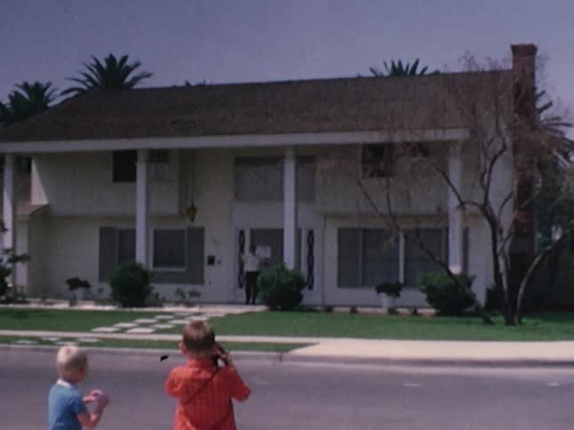 Two boys standing outside looking at a man exiting the house