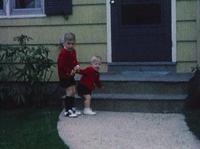 A young boy holding a toddler's hand and walking him up and down a sidewalk