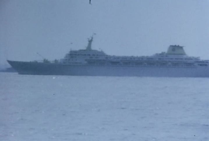 Large ships can be seen in the distance moving on a cloudy day