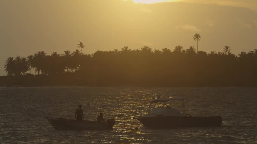 Two people on a boat pull another boat behind it