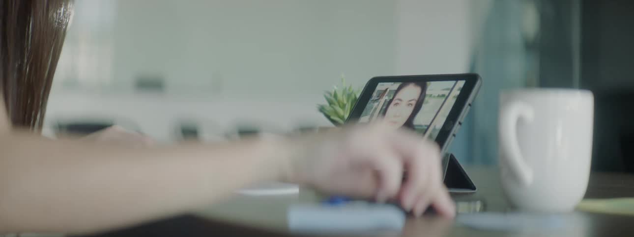 A woman writes on a piece of paper while video chatting with another woman on a tablet