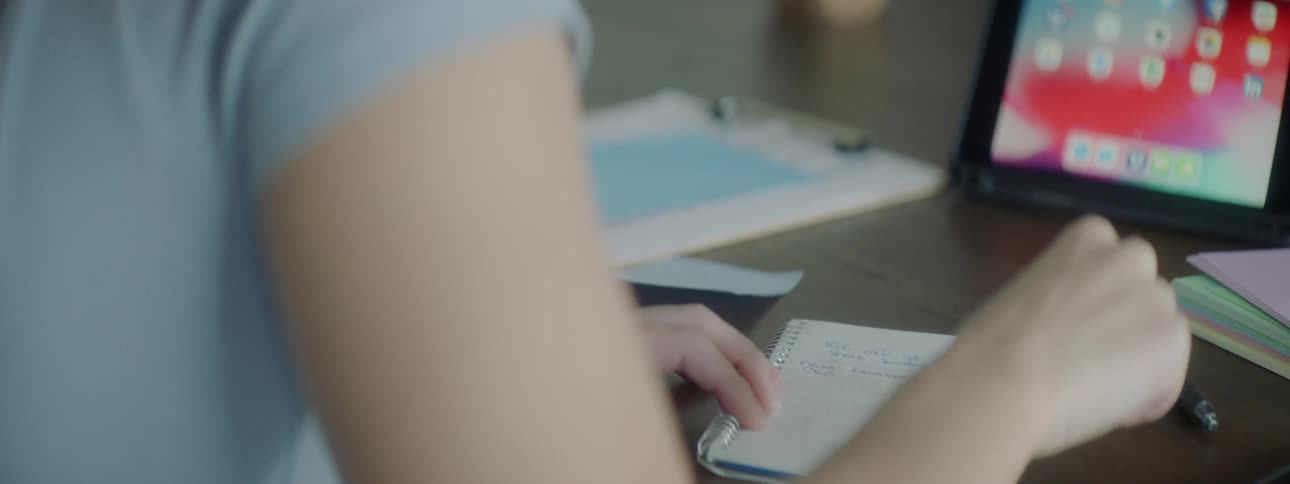 A woman works at a desk with notepads and a tablet