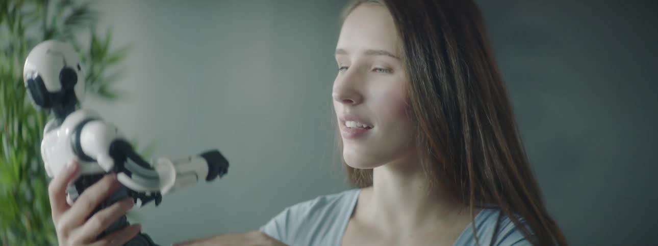 A woman holds a toy robot and inspects it carefully
