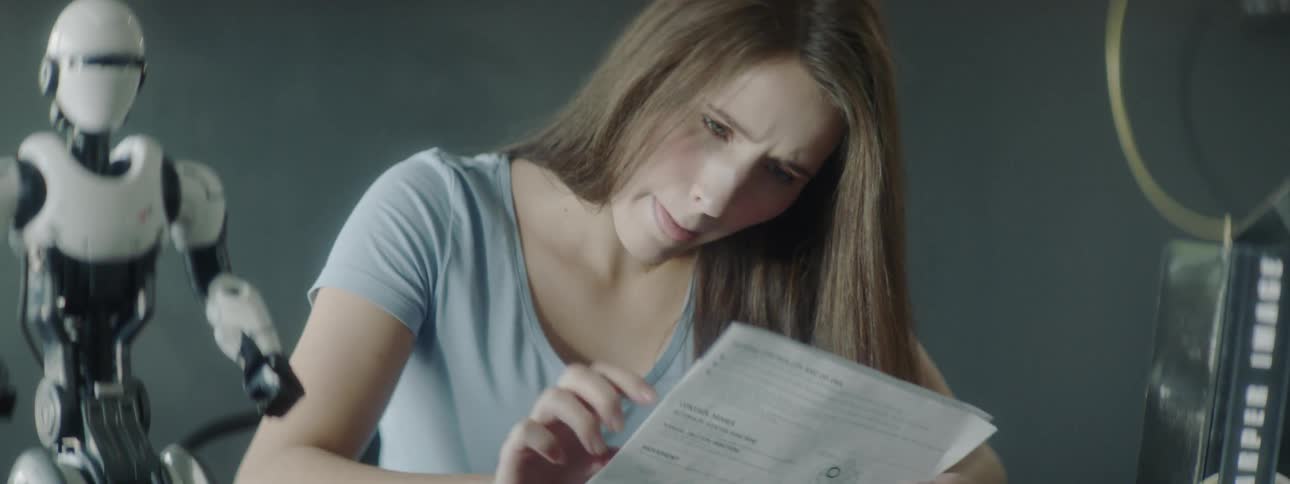 A woman sits at a table reading an instruction sheet for a small robot