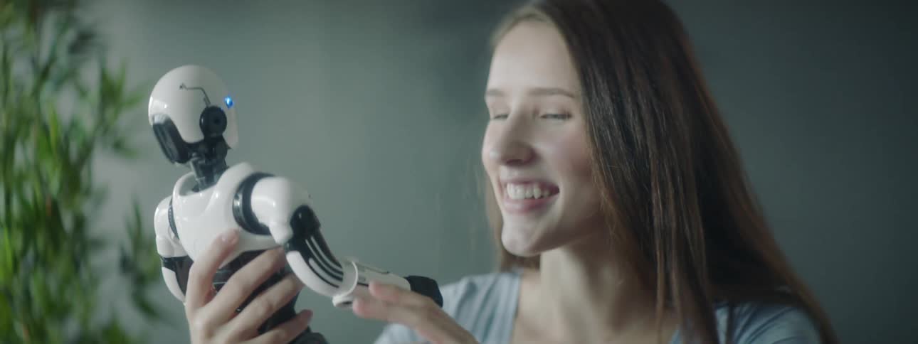 A woman holds a toy robot and places it on the table in front of her