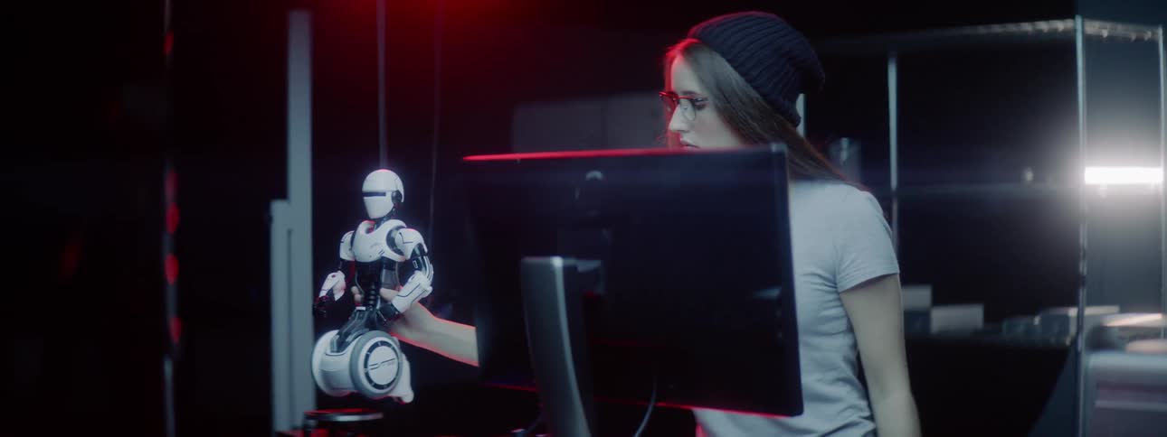 A woman places a toy robot on to a table then turns to face a computer