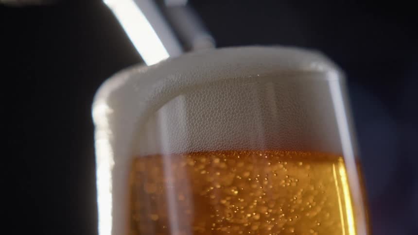A beer glass with bubbles overflowing from it with a beer tap in the background