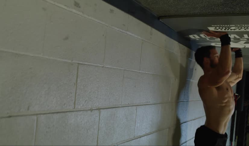 A shirtless man does a handstand and then does pushups against the wall