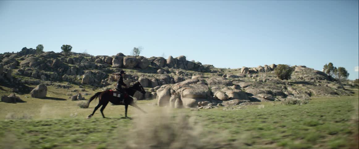 A woman rides a horse through a boulder strewn field