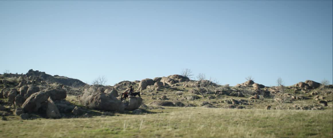 A person riding on a horse navigates through a rocky terrain near a open grassy field