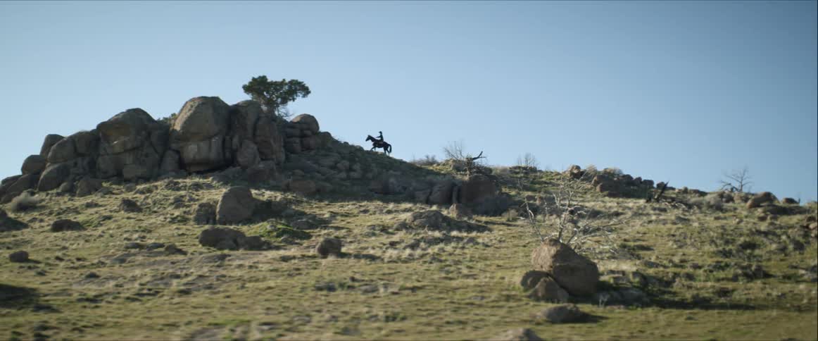A person on a horse stand on top of a large rocky hill