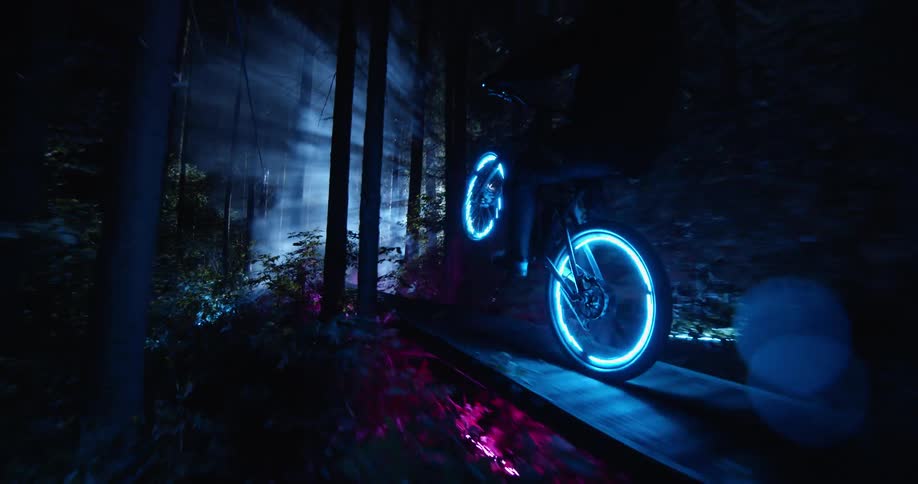 Bicyclist rides across raised wooden walk in forest through spotlight