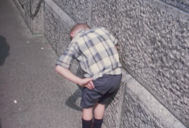 A boy leans over next to a wall