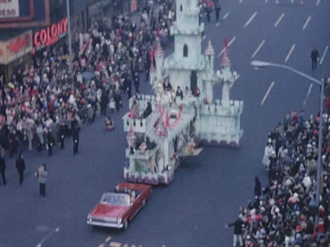 A parade float is driven down the road by a red car
