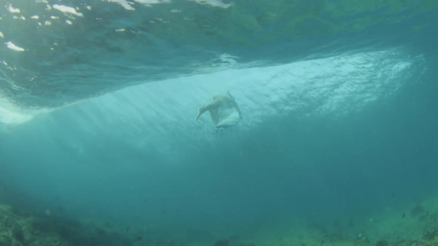 A surfer diving under a wave as seen from underwater
