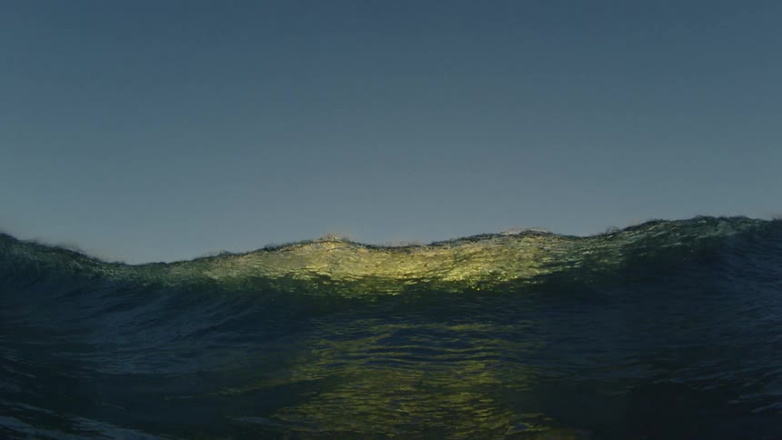 A large wave curls over and crashes down as it is seen from beneath the surface of the ocean