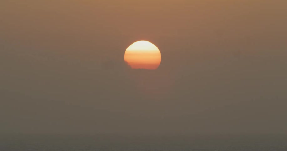 Sun sets in cloudy orange tinted sky