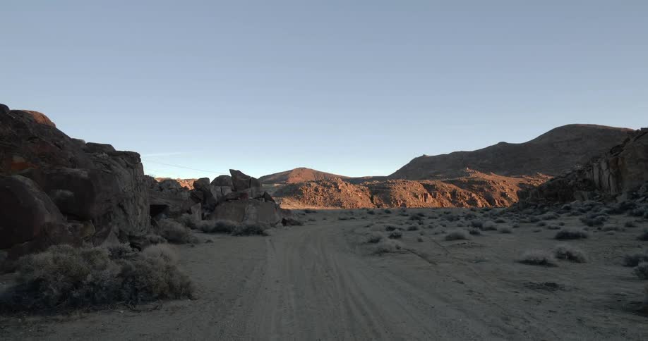 A dirt trail is marked by numerous tire tracks as it curves through a desert landscape lined by mountains