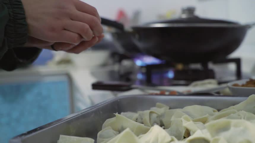 A person grabs prepared dumplings from a pan and readies to cook them