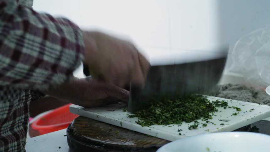 Man chopping cilantro with a cleaver on a white cutting board