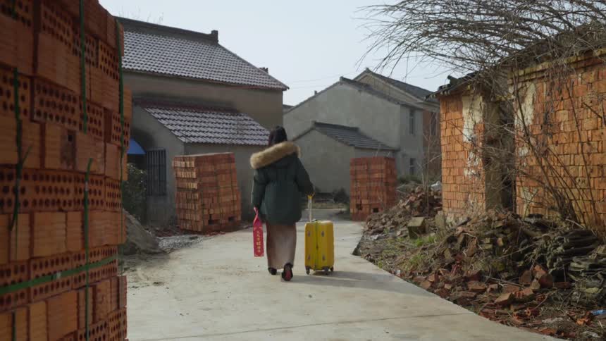 Woman in a parka walking with a wheeled suitcase and carrying a red bag